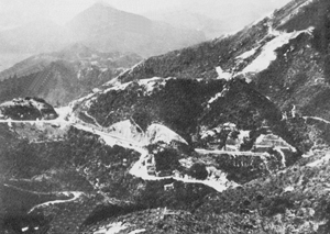 Wong Nei Chong Gap, scene of one of the fiercest encounters in the battle for Hong Kong. Here a company of the Winnipeg Grenadiers held out for several days and inflicted much delay and many casualties upon the Japanese. The Island's main north-south road runs from right to left across the picture. <em>(Canadian War Museum J-2055312)</em>