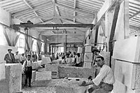 Ouvriers au travail sur des blocs de pierre équarris et numérotés dans un hangar.