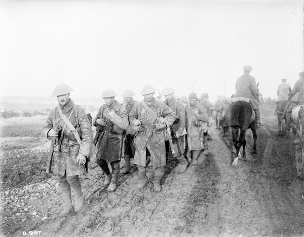 Plusieurs soldats marchant deux par deux, leurs manteaux sont sales de boue.