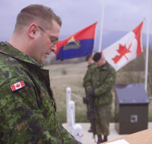 Un soldat lisant un texte pendant une cérémonie et deux soldats en position de recueillement.