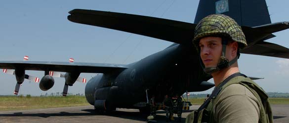 Un membre des Forces armées canadiennes monte la garde près d'un avion Hercules alors que l'équipage décharge l'appareil.