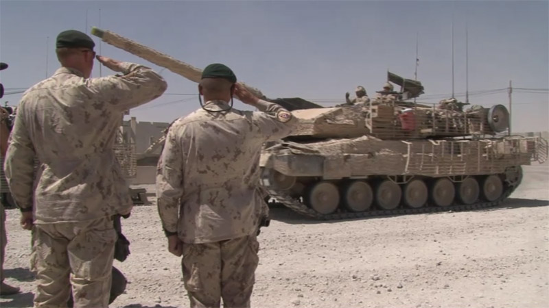 Des soldats canadiens au salut au passage de chars d’assaut en Afghanistan.