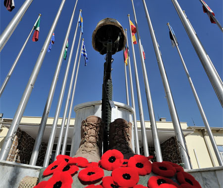 Un casque militaire canadien, un fusil C7, des plaques d’identité, des bottes de militaire et une rangée de coquelicots sont disposés devant le monument