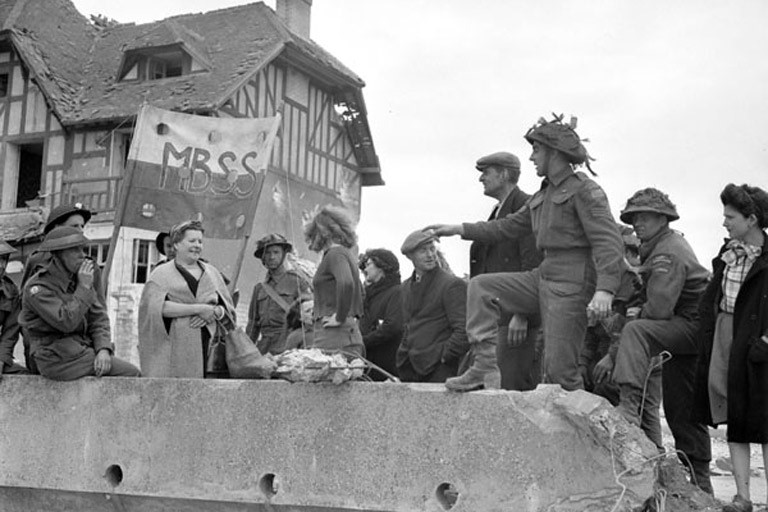 Canadian soldiers speak to liberated French citizens in the village of Bernières-sur-Mer, France, in June 1944. The house that became known as “Canada House” is seen in the background. 