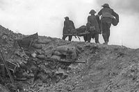 Stretcher bearers carrying a wounded man over the top of a trench.