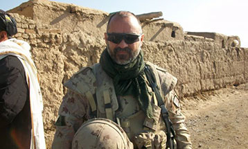 Bruno Plourde in military camouflage uniform, standing in front of a compound in Afghanistan.