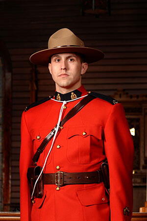 A portrait of Bryan Martell. He is wearing a red Mountie uniform and brown hat, and is standing in a room with brown walls.